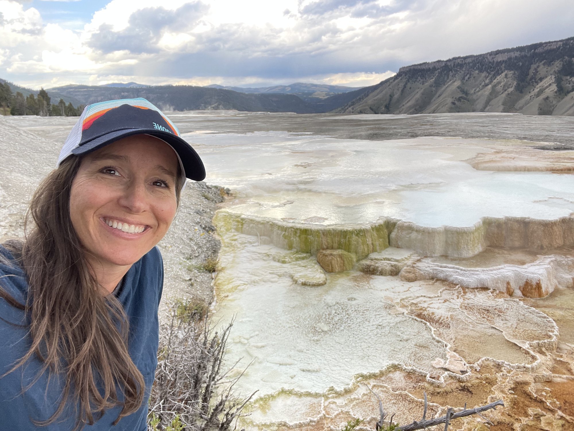 Dr. Rachel Quinn smiling outdoors at Yellowstone National Park, with travertine terraces and mountains behind her